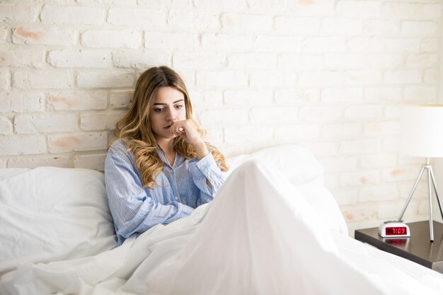 Foto gratuita giovane donna preoccupata che pensa a qualcosa di importante mentre è seduta a letto al mattino