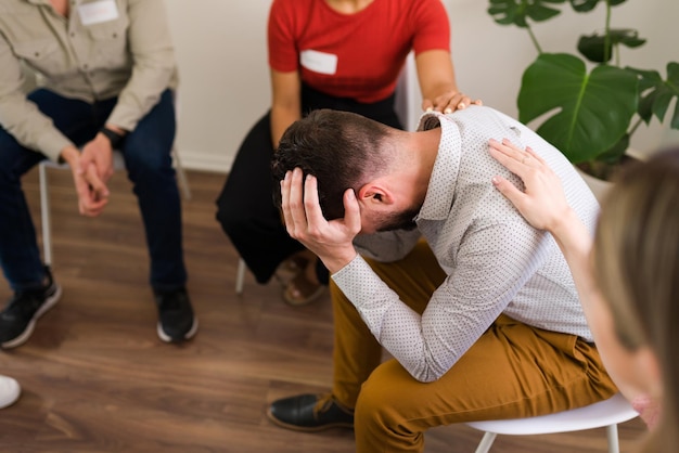 Don't worry, everything is going to be ok. Members of an AA or support group comforting a sad hispanic man and offering mental health advice