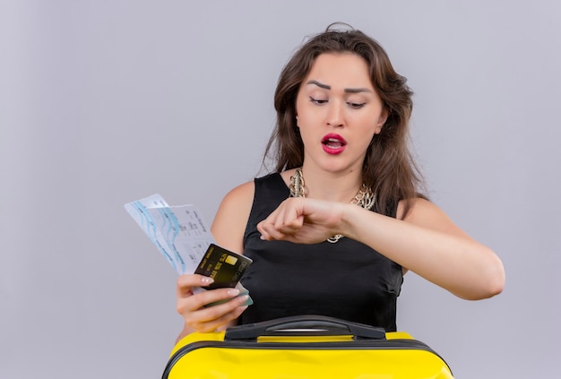 Worrynig traveler young girl wearing black undershirt holding tickets and bank card on white background