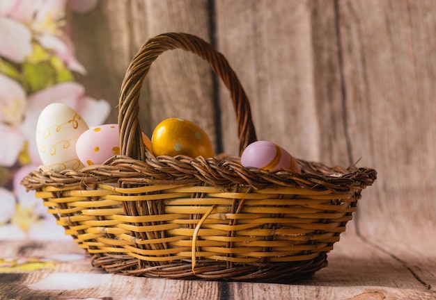 Woven basket filled with colorful Easter eggs on a wooden surface decorated with artificial foliage