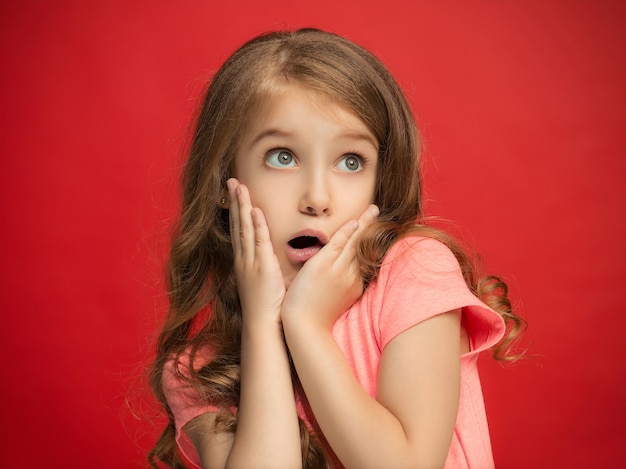 Foto gratuita wow. bello ritratto frontale femminile isolato sul backgroud rosso dello studio. giovane ragazza teenager sorpresa emotiva in piedi con la bocca aperta. emozioni umane, concetto di espressione facciale. colori alla moda