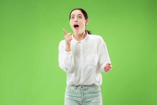 Wow. Beautiful female half-length front portrait isolated on green  backgroud. Young emotional surprised woman standing with open mouth