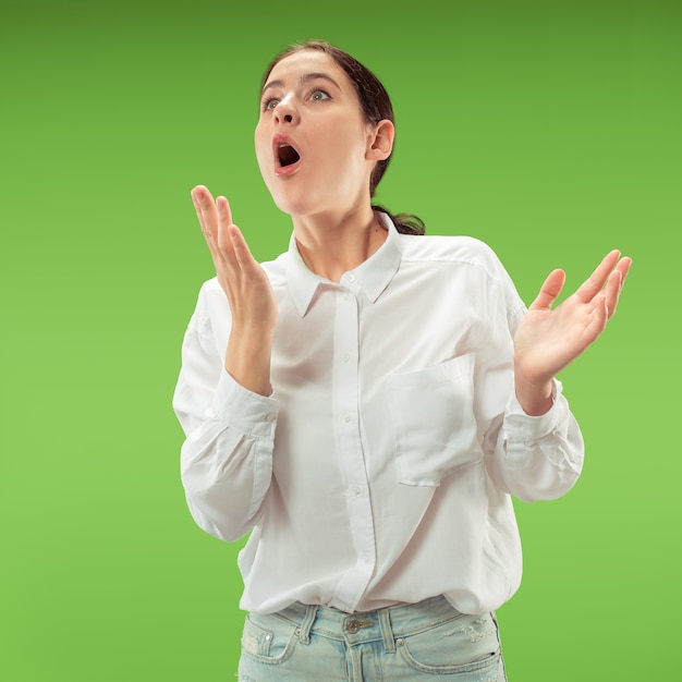 Wow. bello ritratto frontale mezzo busto femminile isolato sul backgroud verde dello studio. giovane donna sorpresa emotiva in piedi con la bocca aperta. emozioni umane, concetto di espressione facciale. colori alla moda