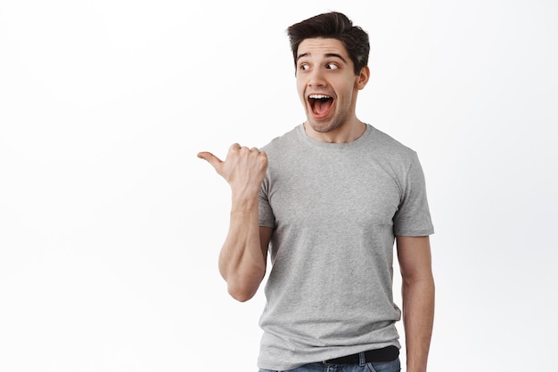 Wow check this out look there Impressed adult man screams from joy and surprise pointing and looking aside at promo offer standing amazed against white background