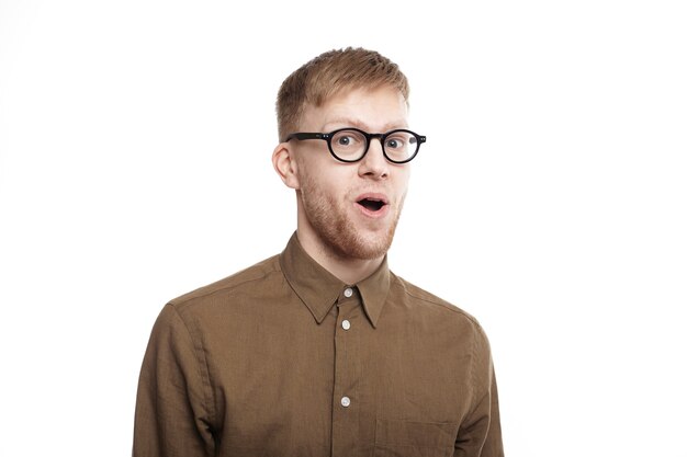 Wow. handsome emotional hipster guy in stylish eyewear staring in full disbelief, raising brows and opening mouth, having completely shocked expression on his hairy face