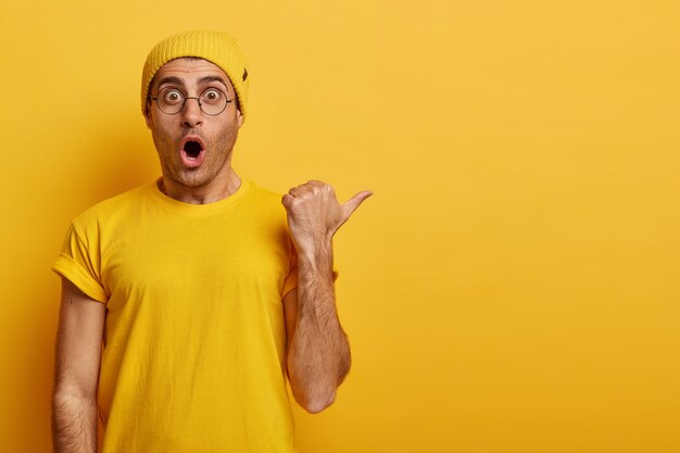 Wow, huge discount opportunity. Emotive guy with terrified face expression demonstrates unexpected opportunity, points thumb right on blank space, wears yellow outfit. Advertisement