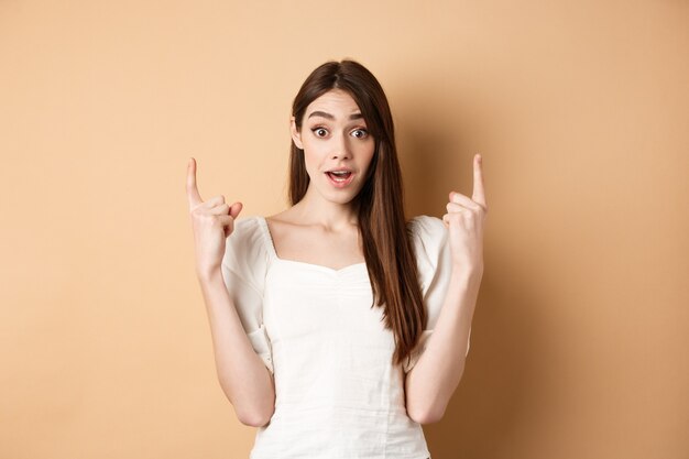 Wow look here amazed cute girl making announcement pointing fingers up and look excited showing prom...