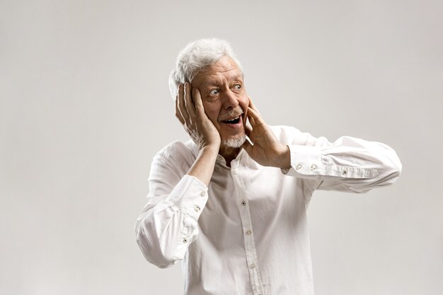 Wow. Senior male half-length portrait on gray wall. Mature emotional surprised bearded man standing with open mouth. Human emotions, facial expression concept. Trendy colors