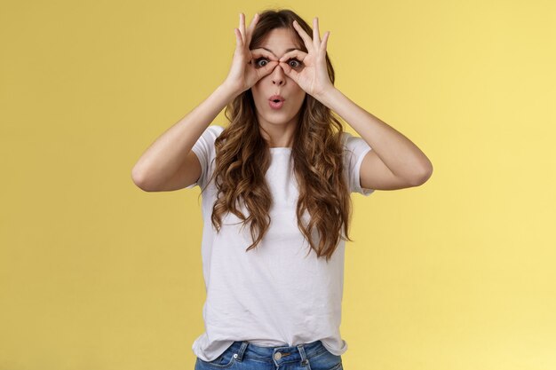 Wow so cool. Girl obersve interesting awesome event show okay perfection gesture look through ring hands folding lips amused wondered glance camera fascinated admiration interested yellow background