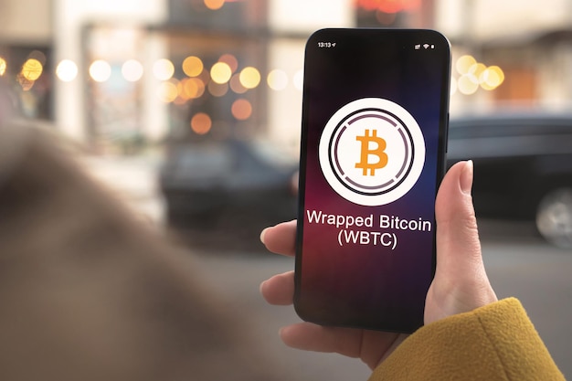 Wrapped bitcoin wbtc cryptocurrency symbol, logo. business and financial concept. hand with smartphone, screen with crypto icon close-up