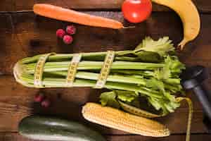 Free photo wrapped celery with vegetables and fruits on wooden table