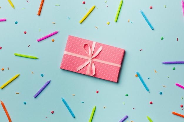 Free photo wrapped gift box around the colorful candles and sprinkles on blue backdrop