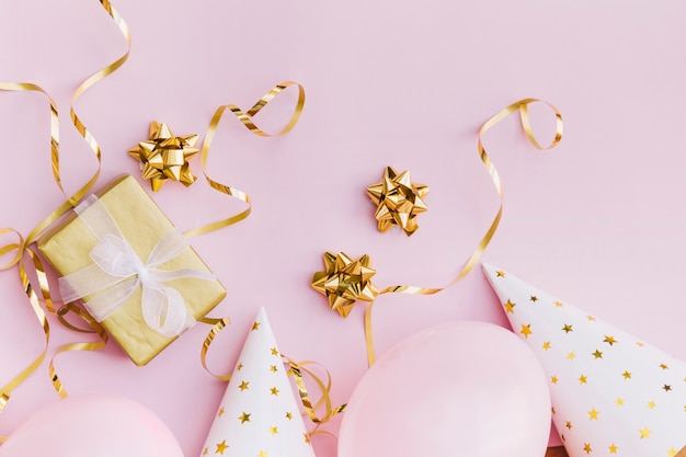 Wrapped gift box; bow; streamer; balloon and party hat on pink background