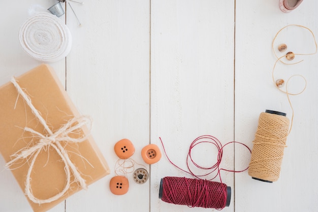 Wrapped gift box; buttons; spool and thimble on white wooden desk