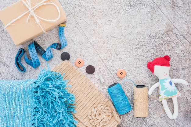 Wrapped gift box; measuring tape; buttons; spool and doll on textured backdrop