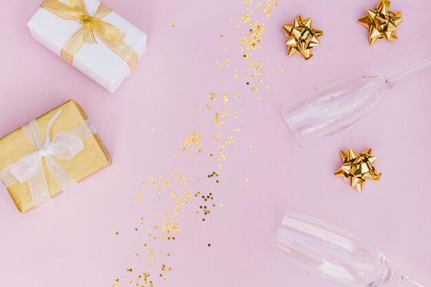 Wrapped gift box with bow; golden confetti; bow and champagne glasses on pink background