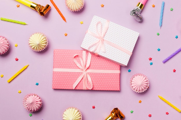 Wrapped gift boxes surrounded with candles; party horn; sprinkles; gift boxes; aalaw on pink background