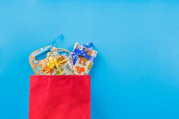 Wrapped gift in red shopping bag over plain backdrop