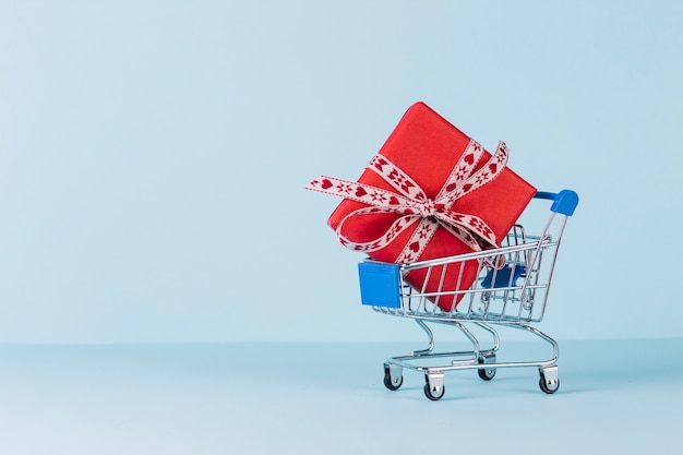 Wrapped red gift box in shopping cart on blue background