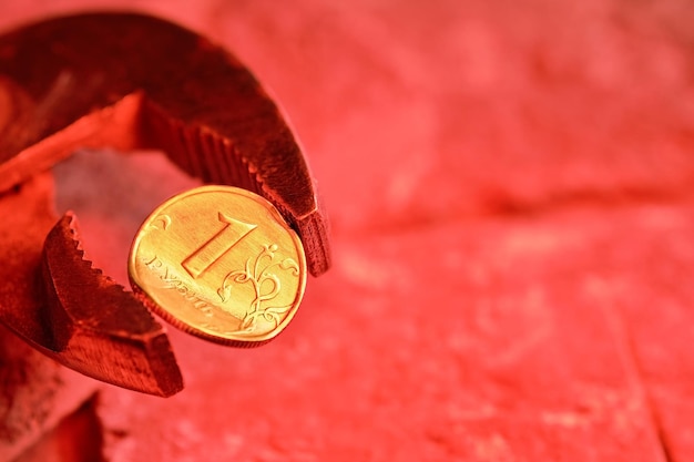 La chiave tiene in una morsa una moneta metallica curva del valore nominale di 1 rublo russo uno sfondo arancione fuoco idea il crollo dell'economia e le sanzioni contro la russia la crisi economica