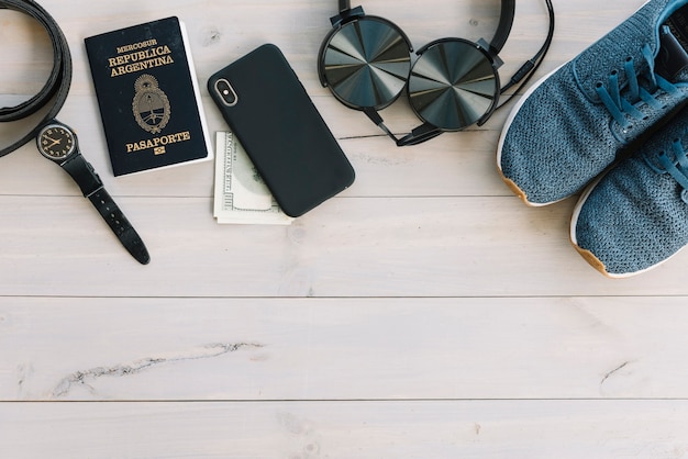 Wrist watch; cell phone; currency; headphone and shoes on wooden table