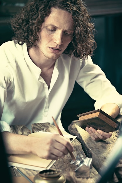 Бесплатное фото Писатель за работой. красивый молодой писатель сидит за столом и что-то пишет в своем блокноте