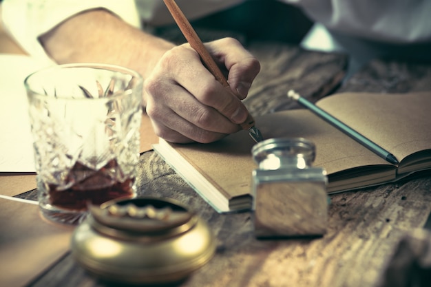 Writer at work. The hands of young writer sitting at the table and writing something in his sketchpad