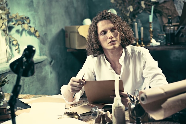 Free photo writer at work. handsome young writer sitting at the table and writing something in his sketchpad at home