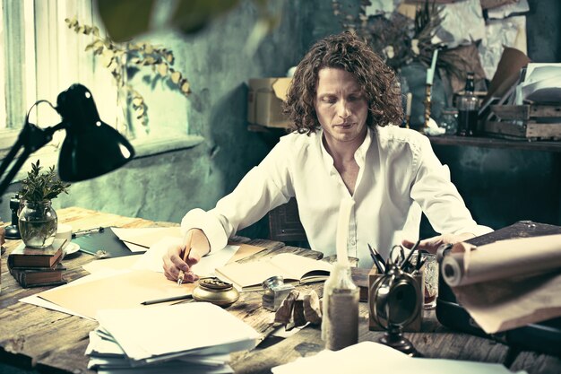 Writer at work. Handsome young writer sitting at the table and writing something in his sketchpad at home