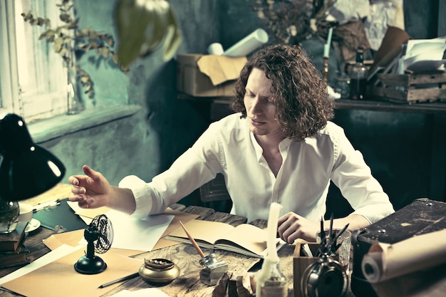 Writer at work. Handsome young writer sitting at the table and writing something in his sketchpad at home