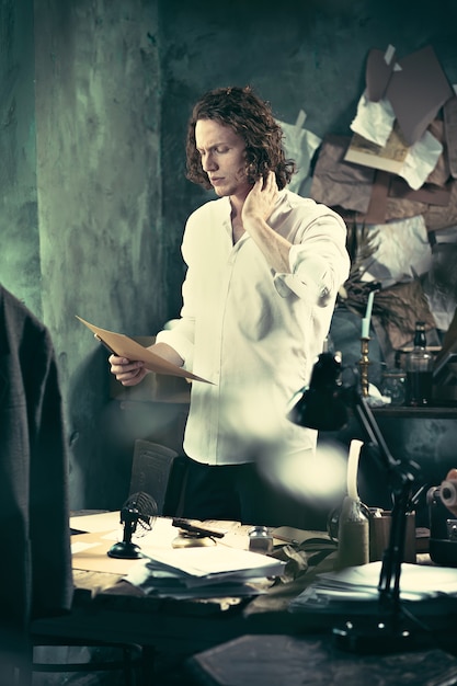 Writer at work. Handsome young writer standing near the table and making up something in his mind at home