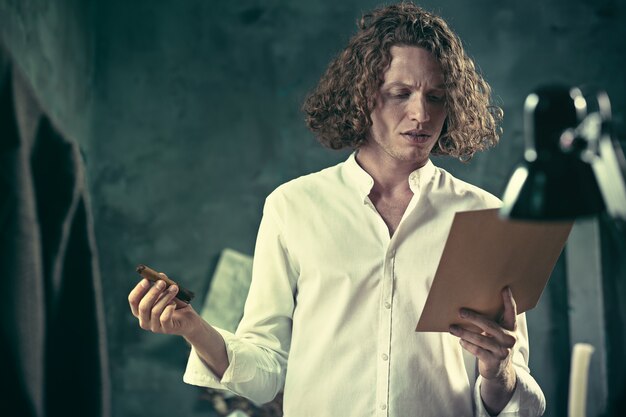 Free photo writer at work. handsome young writer standing near the table and making up something in his mind at home