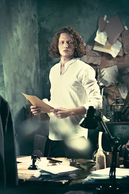 Writer at work. Handsome young writer standing near the table and making up something in his mind