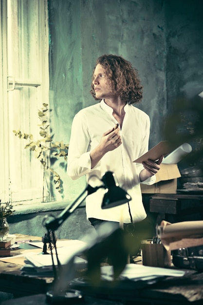 Writer at work. Handsome young writer standing near the table and making up something in his mind