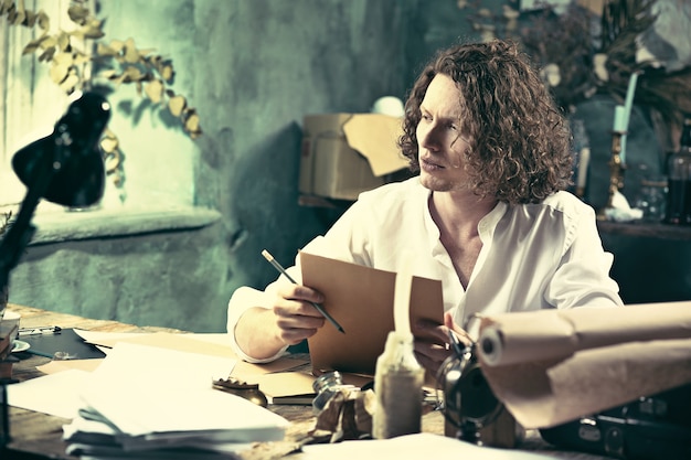 Writer at work. Young writer sitting at the table and writing something in his sketchpad at home