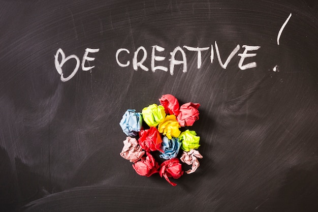 Free photo written creative text over the colorful crumpled paper balls on chalkboard