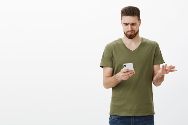 Free photo wtf this emoji mean. confused gloomy and troubled attractive boyfriend frowning as looking upset and clueless at smartphone screen shrugging lifting hand in dismay, trying understand what written