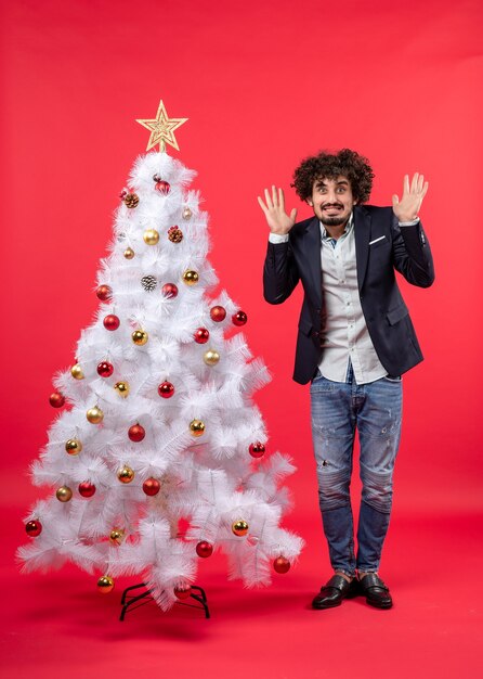 Celebrazione di natale con il giovane barbuto che si sente terribilmente spaventato da qualcosa e in piedi vicino all'albero di natale