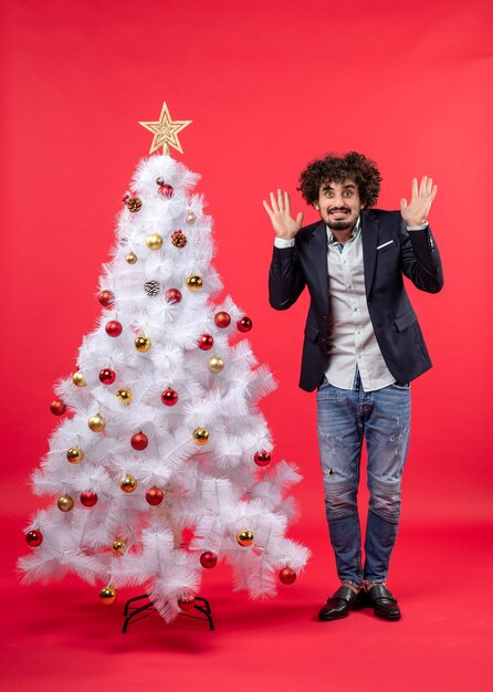 Xmas celebration with bearded young man feeling terribly scared of something and standing near Christmas tree
