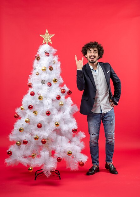 Рождественский праздник со счастливым возбужденным молодым человеком, показывающим жест победы и стоящим возле елки