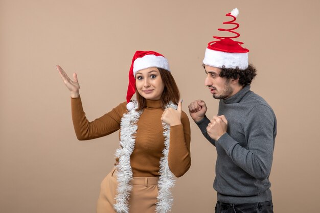 上を指す赤いサンタクロースの帽子をかぶって興奮したクールな素敵なカップルとクリスマス気分