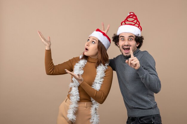 위를 가리키는 빨간 산타 클로스 모자를 쓰고 흥분된 시원한 만족스러운 사랑스러운 커플과 함께 크리스마스 분위기