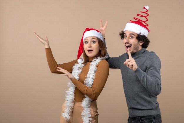 xmas mood with excited cool satisfied lovely couple wearing red santa claus hats pointing above