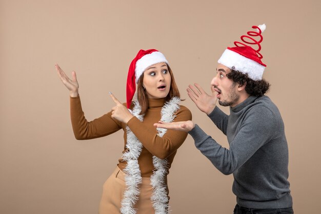 xmas mood with excited cool satisfied shocked lovely couple wearing red santa claus hats pointing above