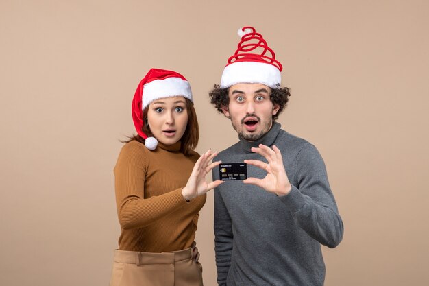 Umore natalizio con coppia cool soddisfatta eccitata che indossa cappelli rossi di babbo natale che mostrano carta di credito