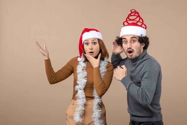 xmas mood with excited satisfied shocked cool couple wearing red santa claus hats pointing above