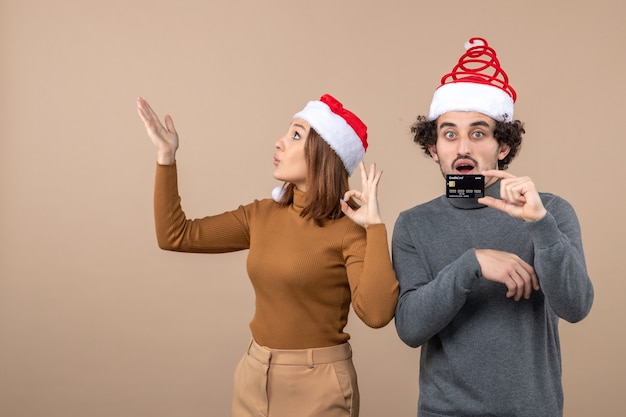 銀行カードを示す赤いサンタクロースの帽子をかぶって興奮して満足している驚いたクールなカップルとクリスマス気分