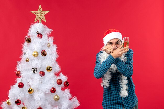 xmas mood with happy crazy emotional young man with santa claus hat in a blue stripped shirt raising a glass of wine near Christmas tree