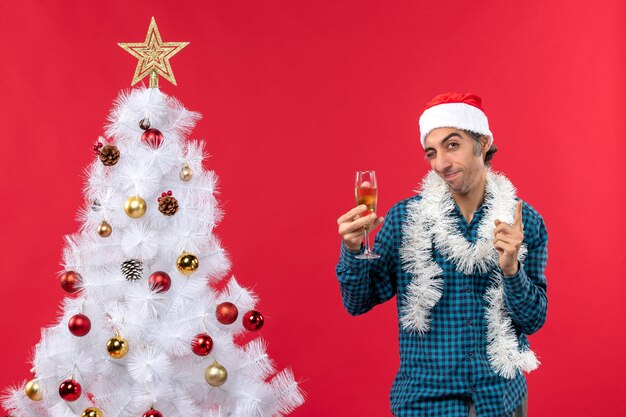 xmas mood with happy crazy emotional young man with santa claus hat in a blue stripped shirt raising a glass of wine near Christmas tree