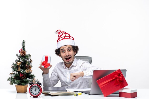 彼の贈り物を保持し、白い背景で彼の時間をチェックするサンタクロースの帽子を持つ神経質な青年実業家とクリスマス気分